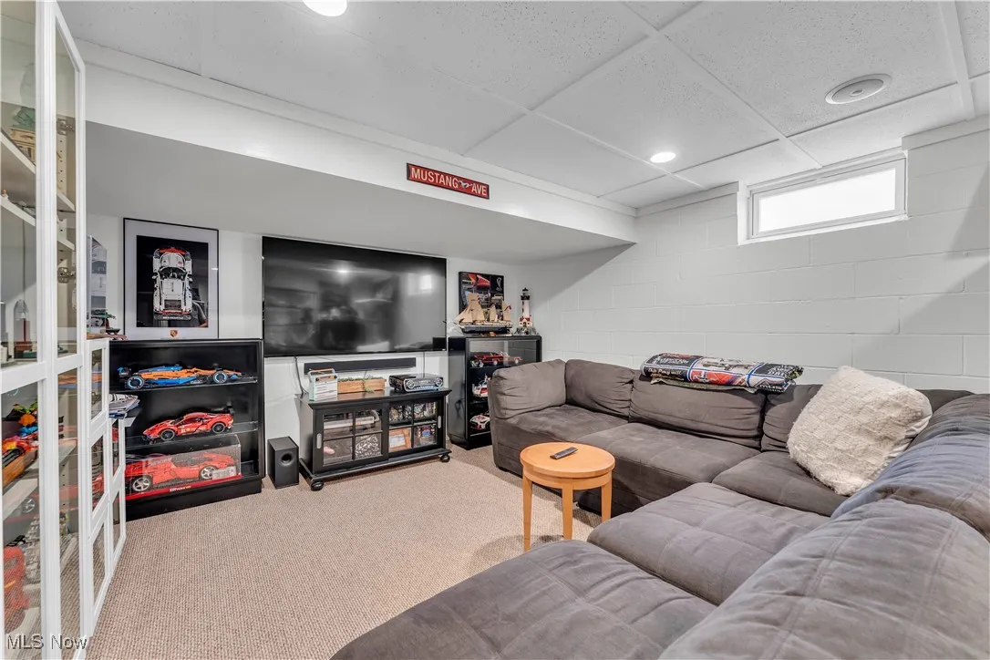 Carpeted basement living room featuring a paneled ceiling, concrete block wall, and recessed lighting