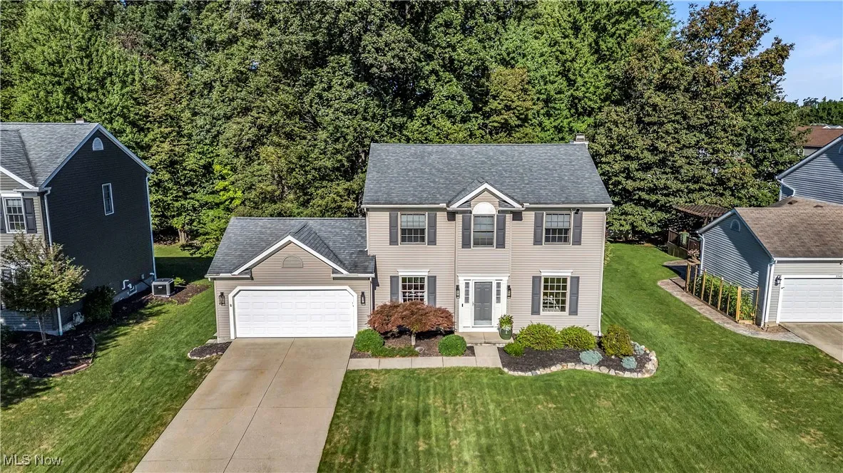 Colonial-style house featuring an attached garage, concrete driveway, a front lawn, and a shingled roof