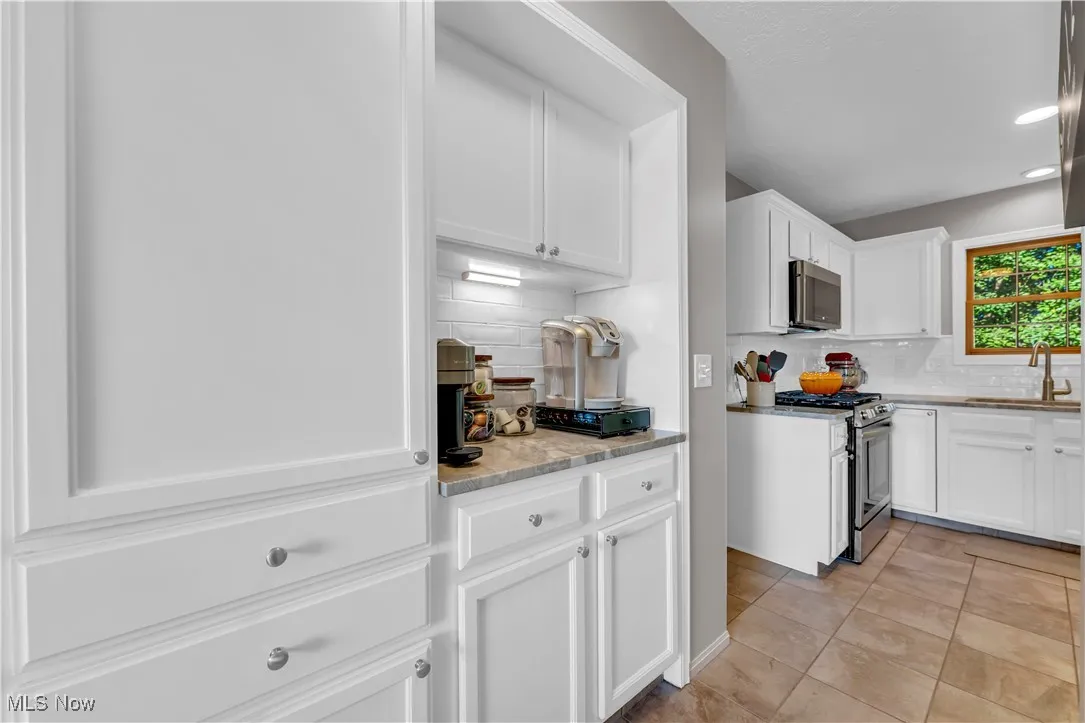Kitchen featuring backsplash, white cabinets, appliances with stainless steel finishes, light stone counters, and recessed lighting