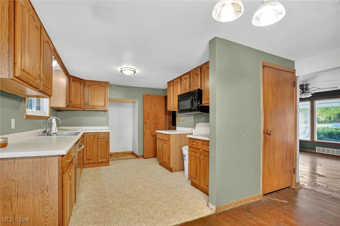Kitchen featuring brown cabinets, light countertops, black microwave, ceiling fan, and stainless steel dishwasher