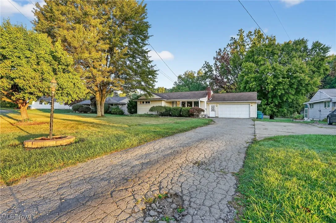 Ranch-style home featuring a front lawn, driveway, a garage, and a chimney