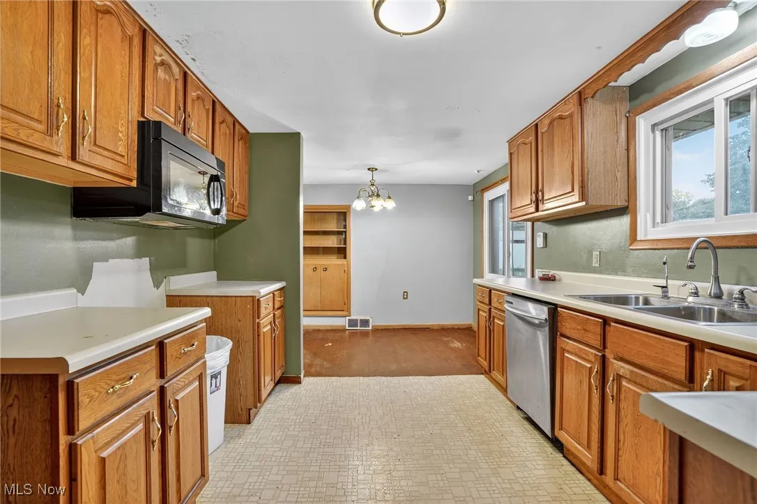Kitchen featuring brown cabinetry, light countertops, a chandelier, stainless steel dishwasher, and black microwave