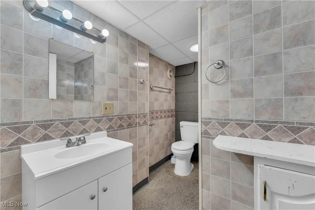 Full bathroom featuring tile walls, vanity, a drop ceiling, and speckled floor