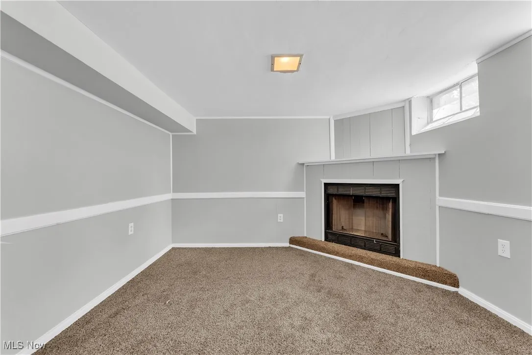 Unfurnished living room featuring a fireplace with raised hearth and carpet