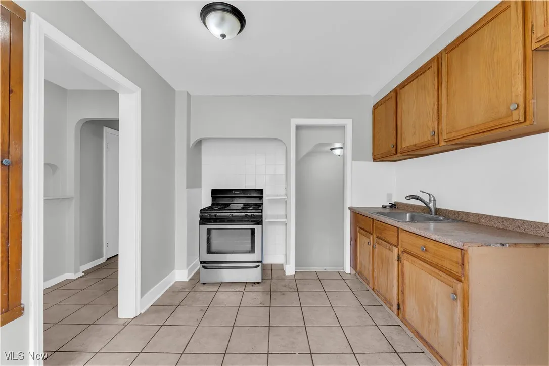 Kitchen featuring gas stove, light tile patterned floors, arched walkways, brown cabinetry, and light countertops