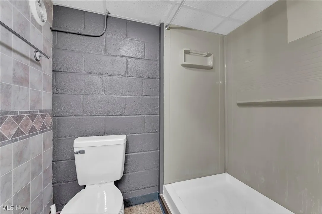Full bathroom featuring concrete block wall, a shower stall, and a paneled ceiling