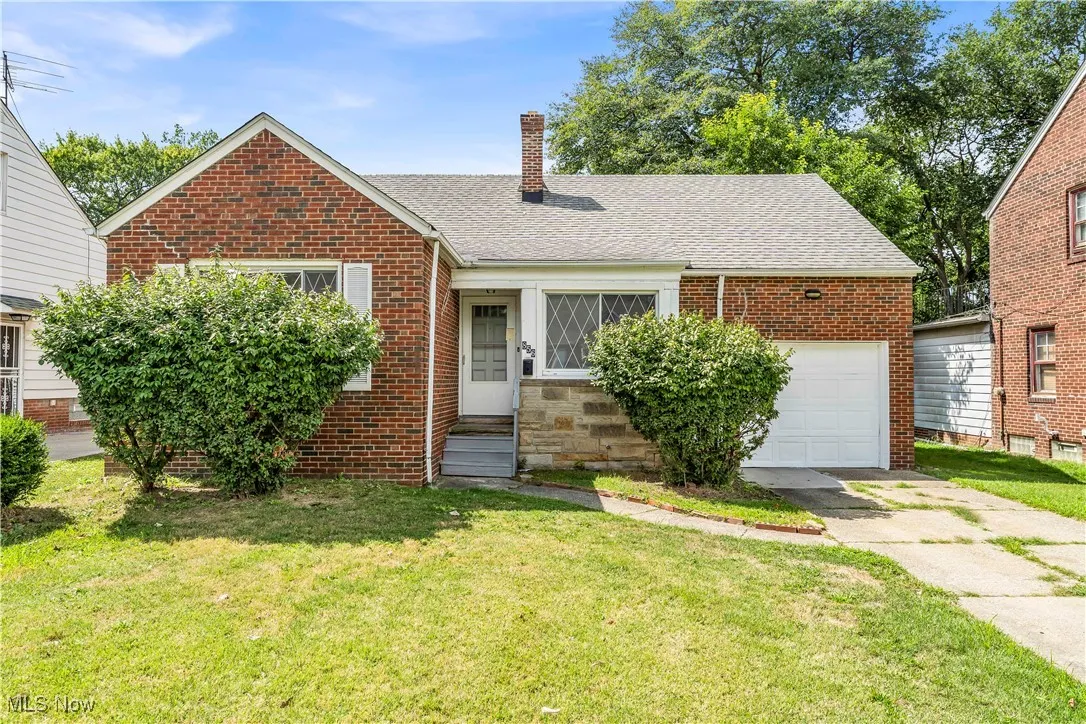 View of front of property featuring a chimney, brick siding, concrete driveway, and a garage
