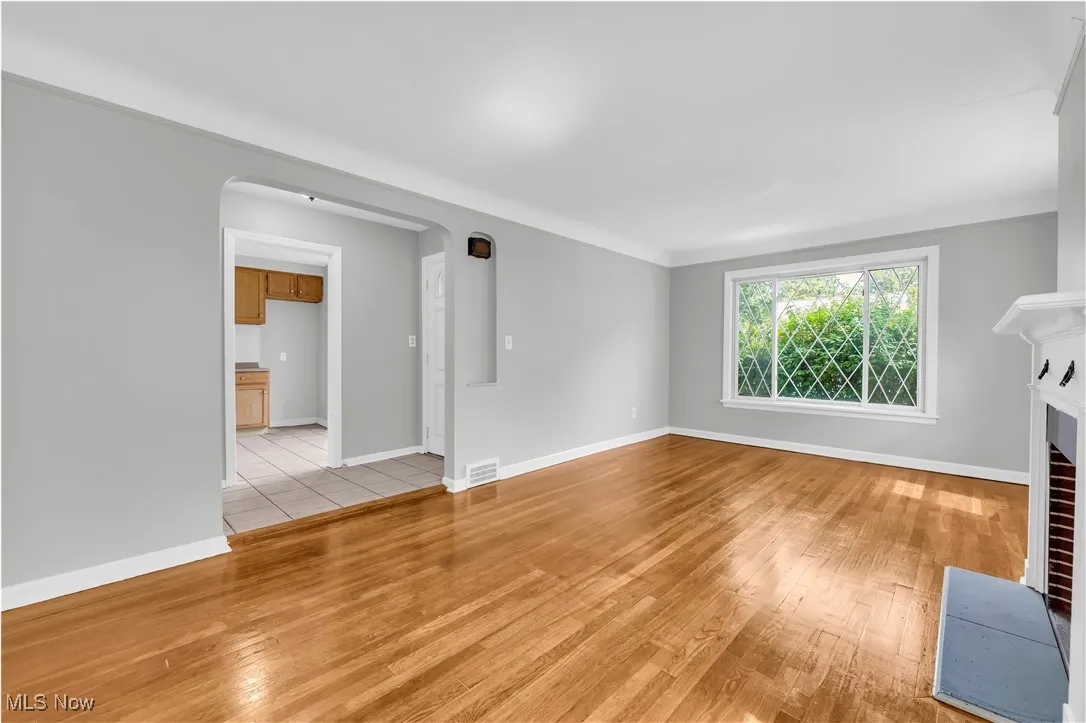 Unfurnished living room with arched walkways, light wood-type flooring, and a fireplace with flush hearth