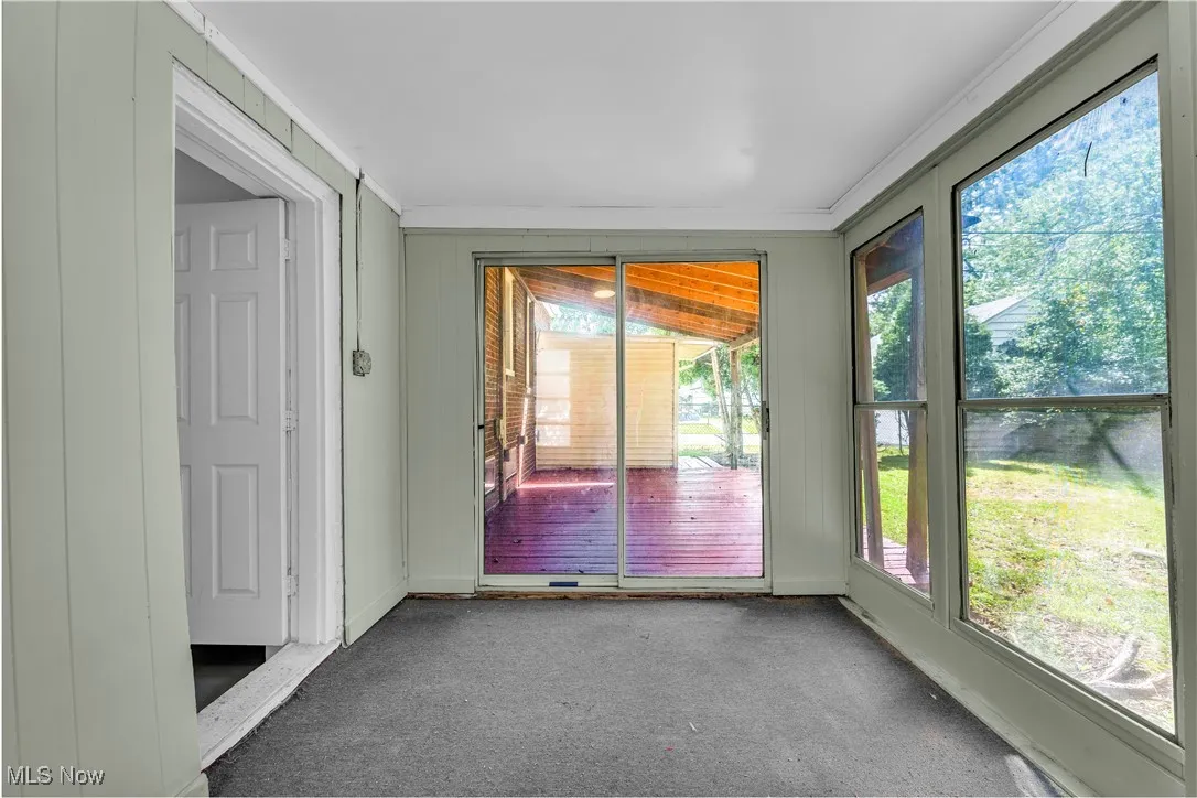 Unfurnished sunroom featuring carpet flooring, wood walls, and ornamental molding