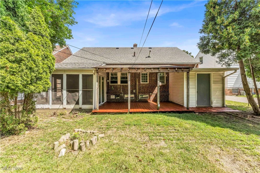 Back of property with a yard, roof with shingles, a deck, a sunroom, and brick siding