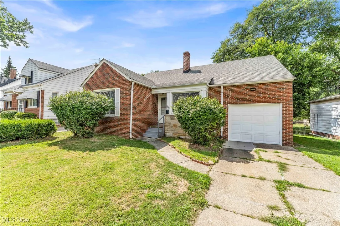 View of front facade featuring brick siding, a front yard, a chimney, and a garage