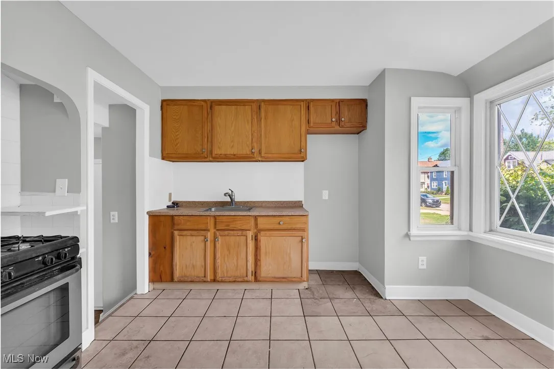 Kitchen with gas stove, light tile patterned flooring, brown cabinetry, and light countertops