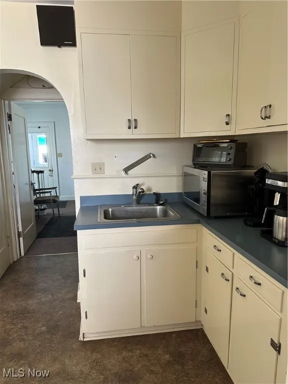 Kitchen / lunchroom with arched walkways, white cabinets, and dark countertops