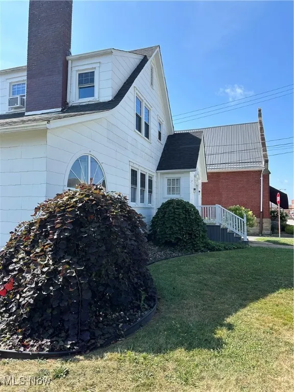 View of side of property featuring a chimney, a yard, and a shingled roof