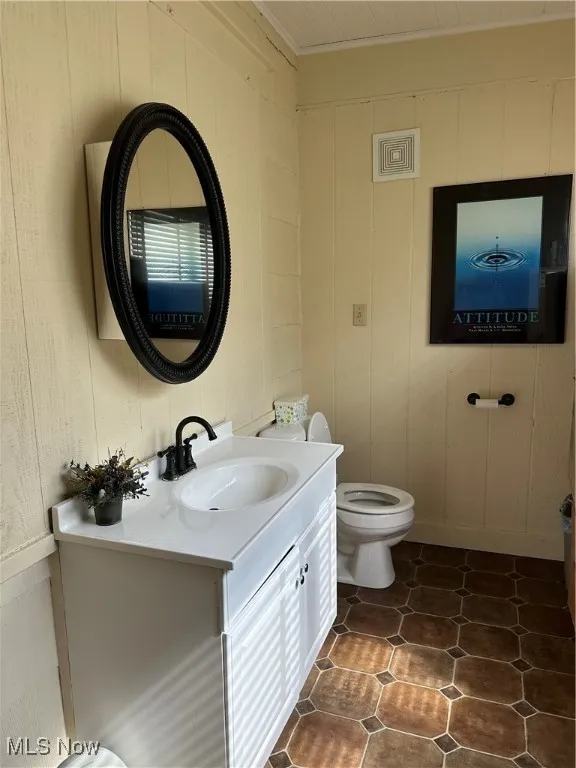 1/2 Bathroom on main level featuring vanity, dark tile patterned flooring, and wooden walls