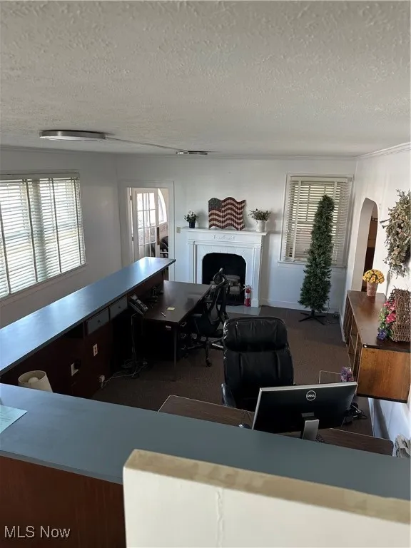 Lobby area featuring a textured ceiling, a fireplace, dark colored carpet, arched walkways, and a desk