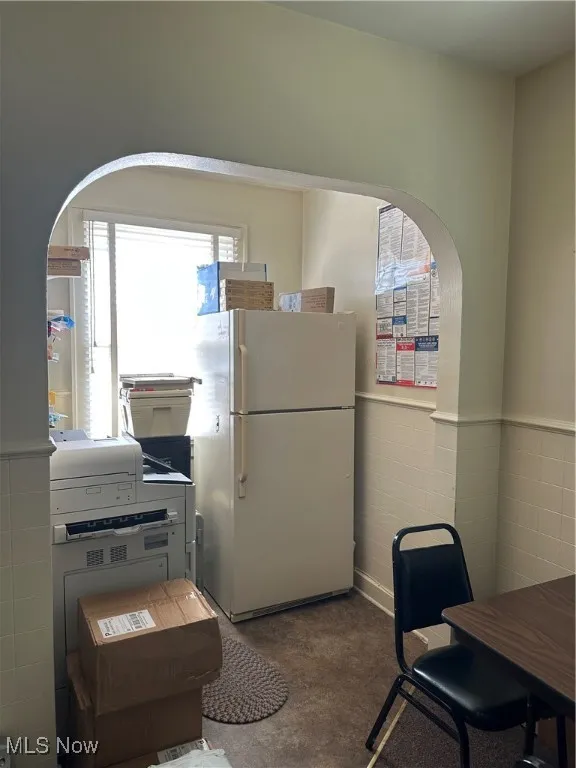 Kitchen/ lunch room featuring wainscoting, freestanding refrigerator, arched walkways, and tile walls