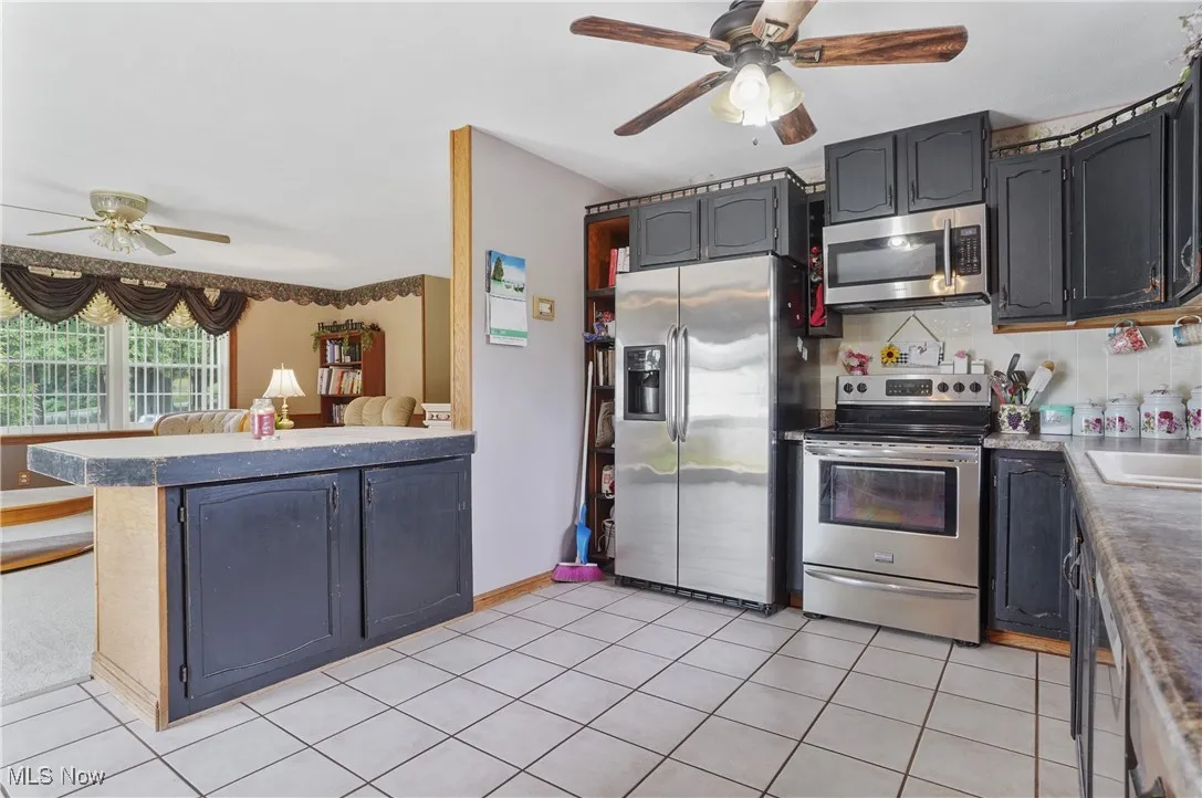 Kitchen featuring ceiling fan, appliances with stainless steel finishes, a peninsula, and light tile patterned floors