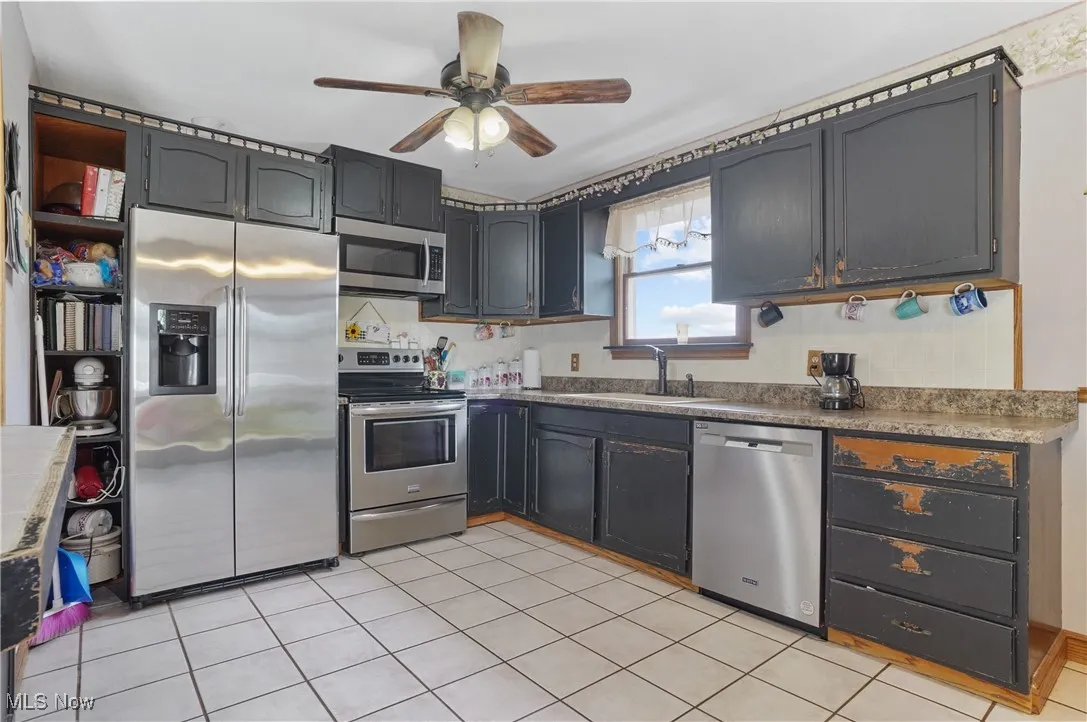 Kitchen with appliances with stainless steel finishes, light tile patterned floors, and a ceiling fan