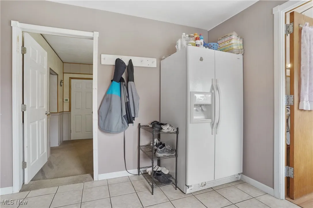 Kitchen with white fridge with ice dispenser, light tile patterned flooring, and light carpet