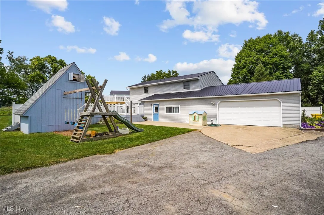 Back of property featuring concrete driveway, a garage, a playground, and a metal roof