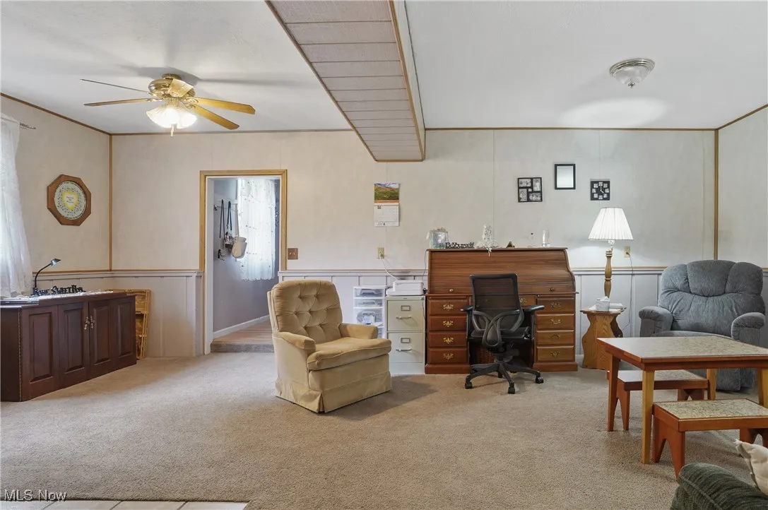 Office space with light colored carpet, a decorative wall, ceiling fan, and a wainscoted wall