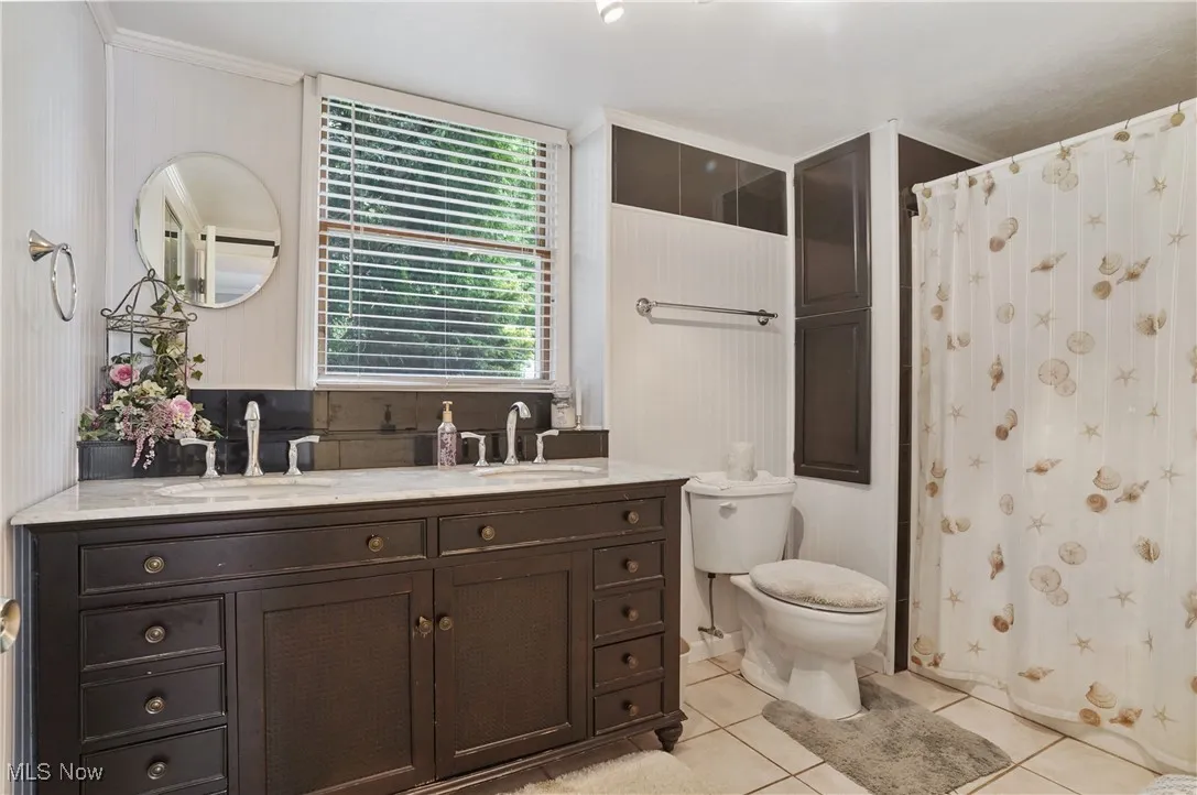 Full bath with light tile patterned floors, double vanity, and a shower with shower curtain