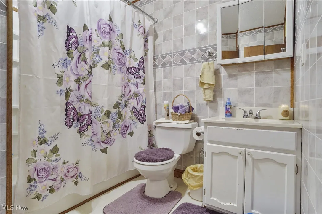 Full bath with tile walls, vanity, shower / bath combo, and tasteful backsplash