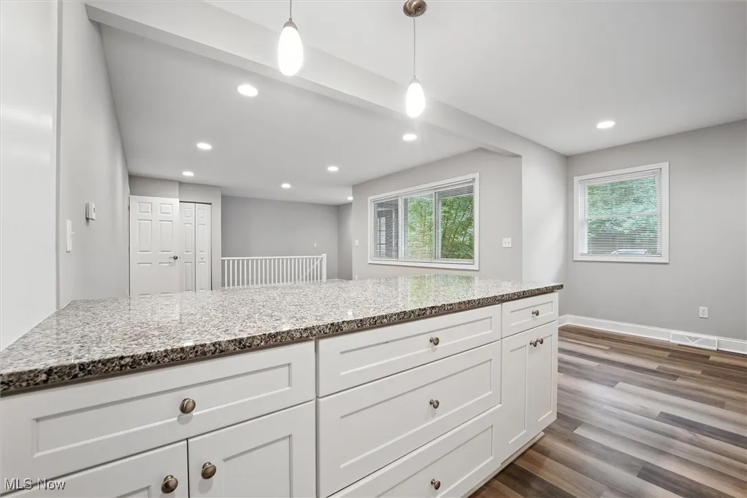 Kitchen featuring pendant lighting, white cabinets, light stone counters, dark wood-style flooring, and healthy amount of natural light