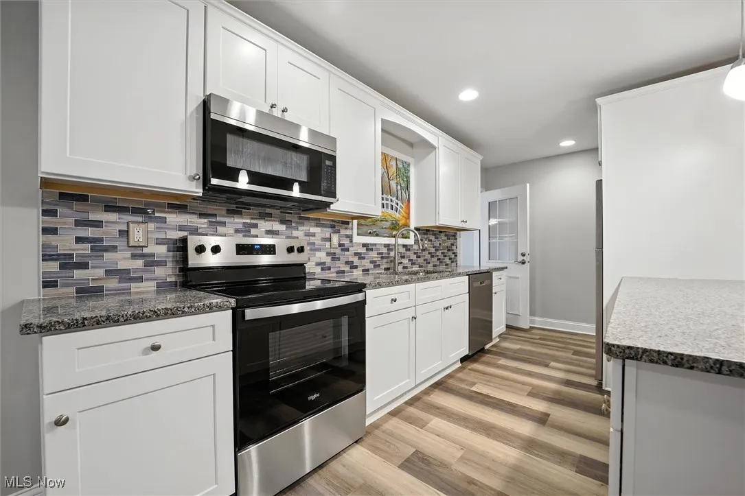 Kitchen with appliances with stainless steel finishes, decorative backsplash, white cabinets, light wood-style flooring, and recessed lighting