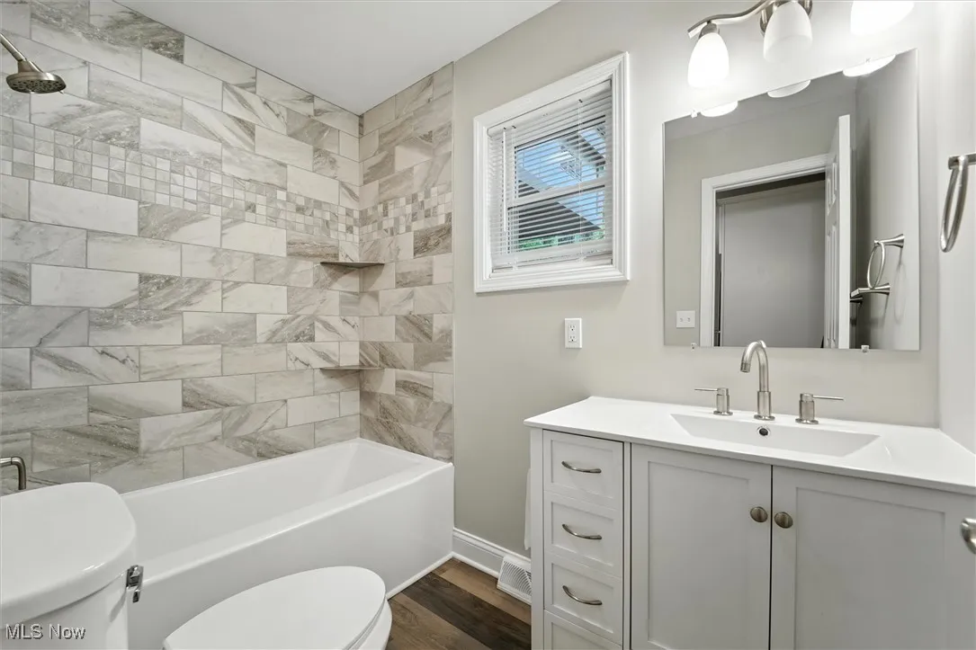 Bathroom featuring vanity, shower / bath combination, and dark wood-style flooring