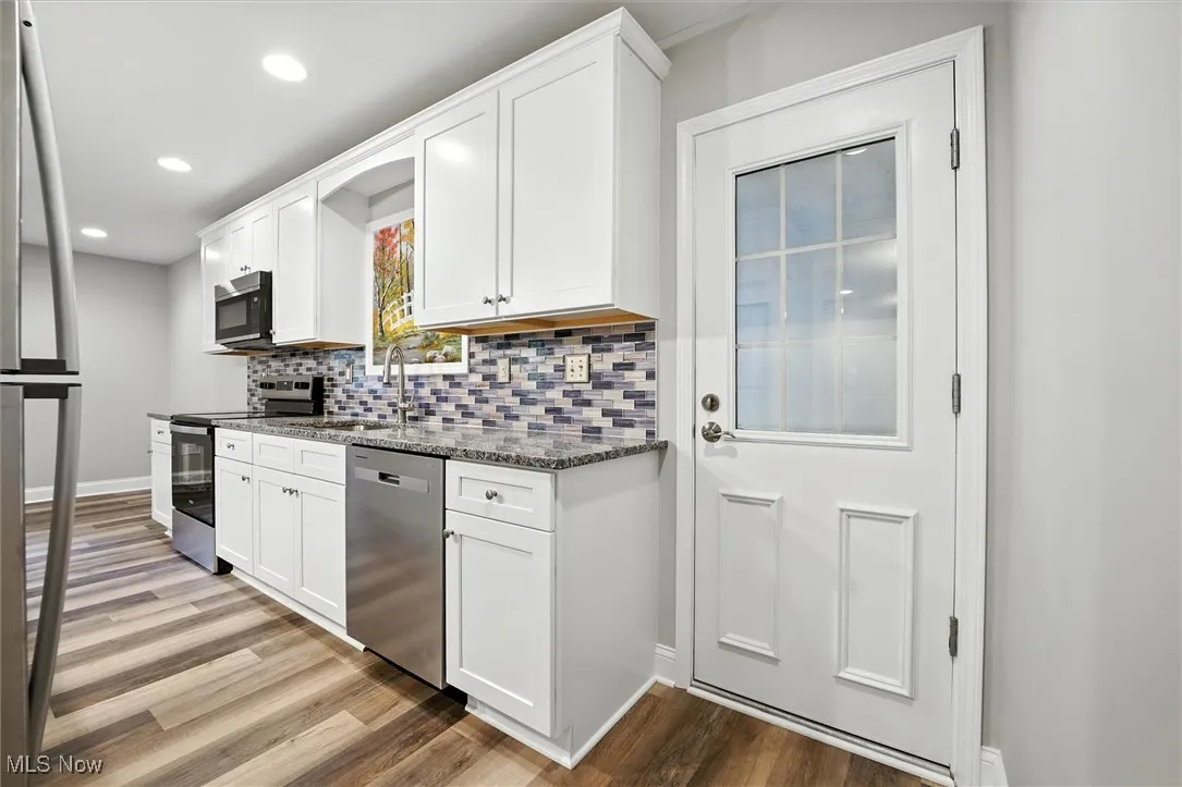 Kitchen featuring dark stone counters, stainless steel appliances, white cabinetry, light wood-style flooring, and tasteful backsplash