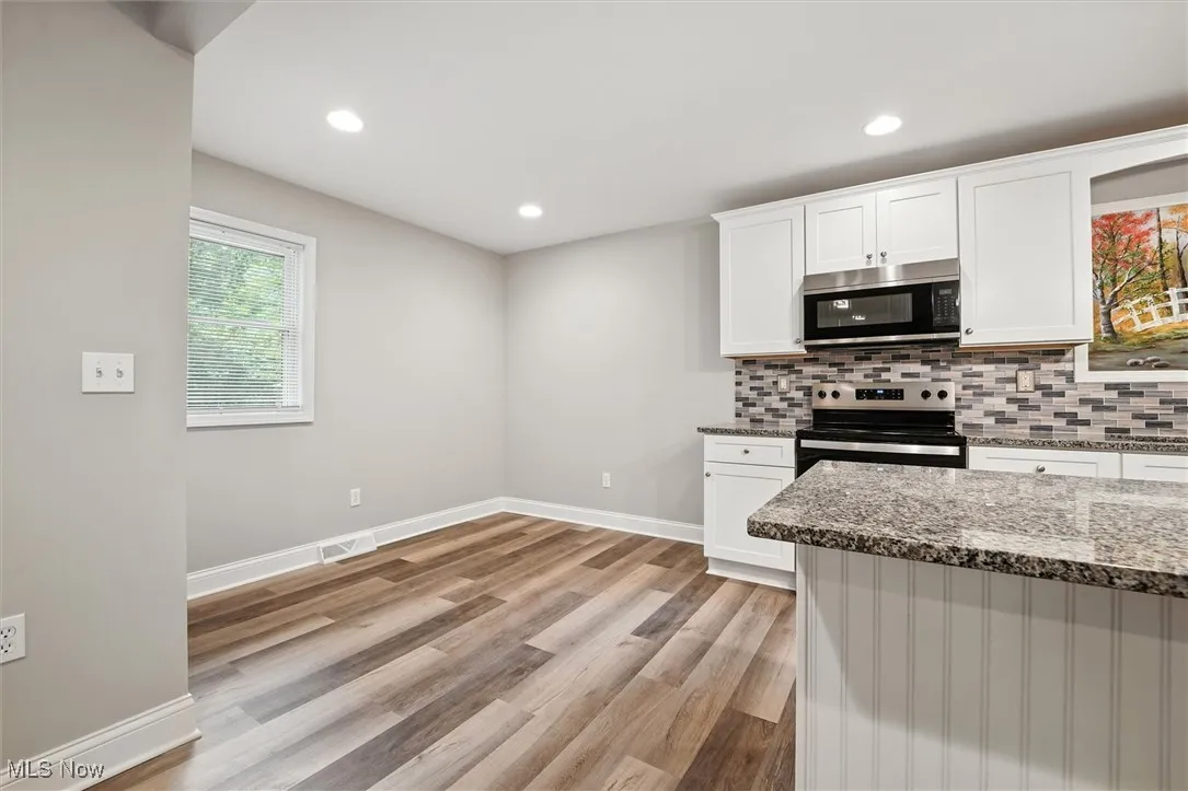 Kitchen with dark stone countertops, appliances with stainless steel finishes, white cabinetry, tasteful backsplash, and recessed lighting