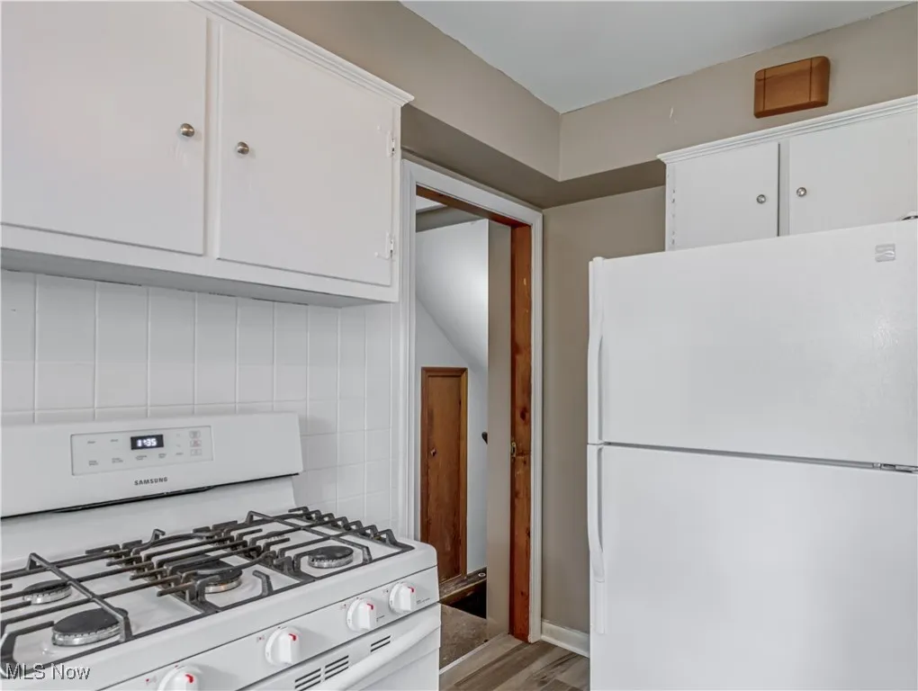 Kitchen with white appliances, white cabinetry, light wood-style floors, and light countertops