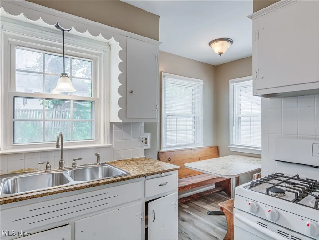 Kitchen with backsplash, white gas range, white cabinets, and light wood-style flooring