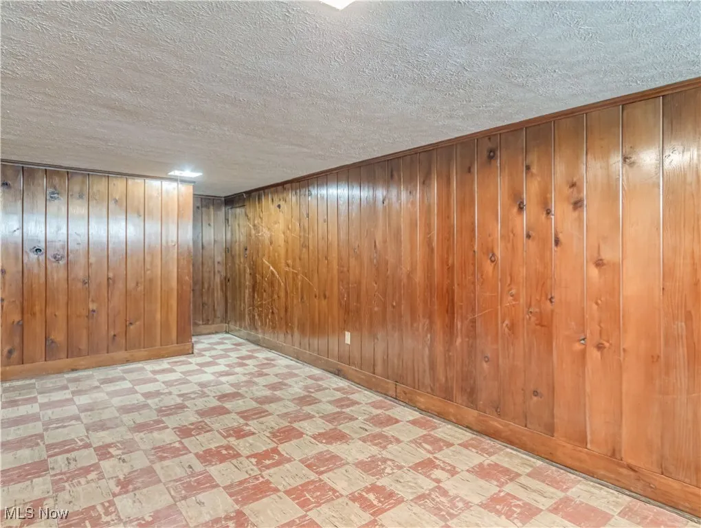 Finished basement with light flooring, a textured ceiling, and wooden walls