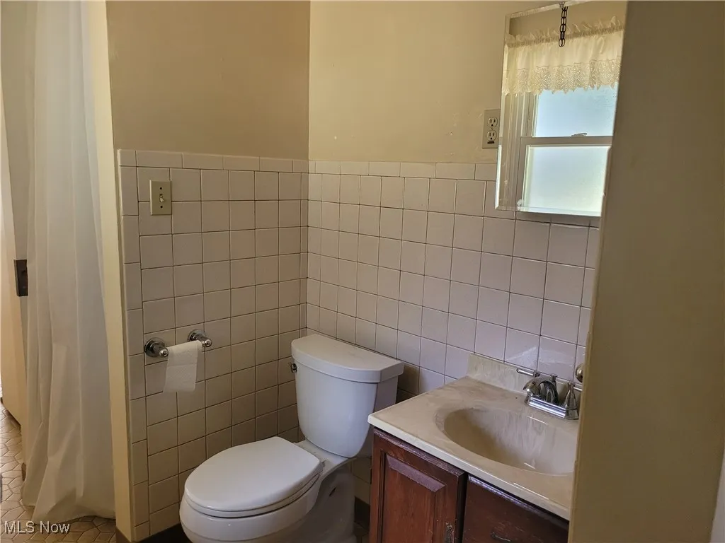 Full bathroom with tile walls, vanity, wainscoting, and a shower with curtain