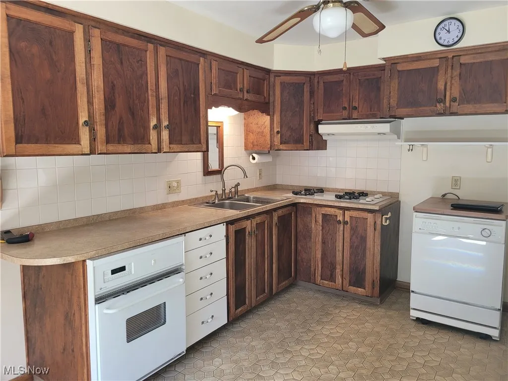 Kitchen with tasteful backsplash, white appliances, a ceiling fan, and light countertops