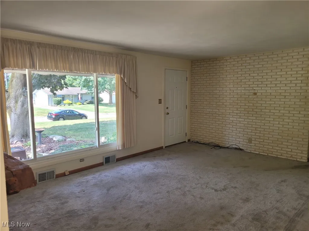 Carpeted empty room with brick wall and baseboards