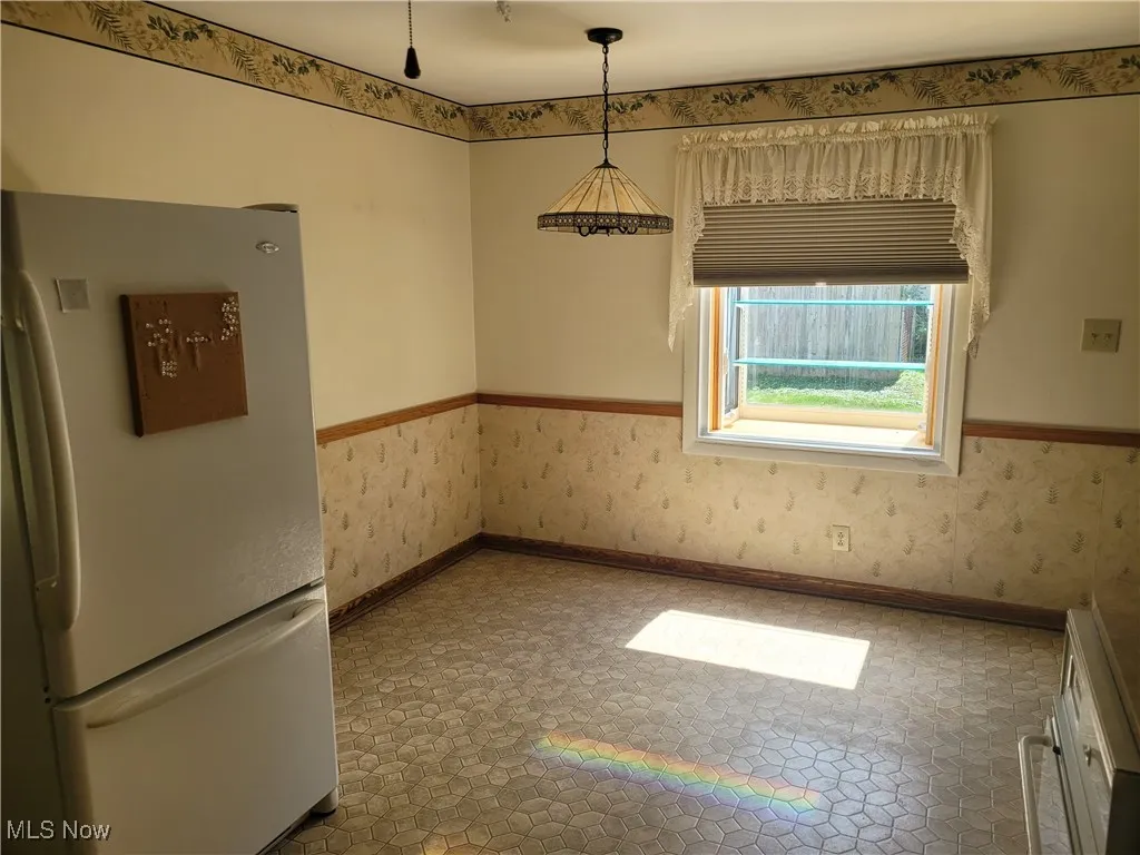 Unfurnished dining area with a wainscoted wall and wallpapered walls