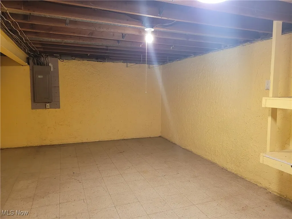 Unfinished basement with tile patterned floors, a textured wall, and electric panel