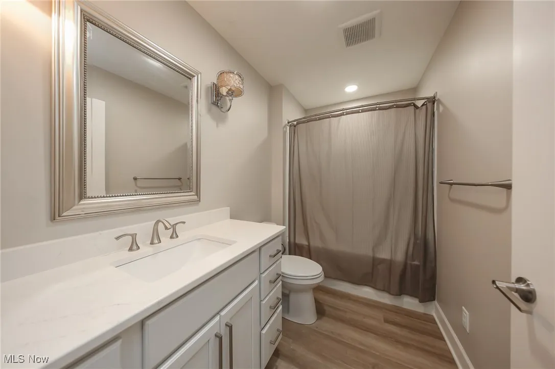 Bathroom featuring vanity, shower / bathtub combination with curtain, light wood-style flooring, and recessed lighting