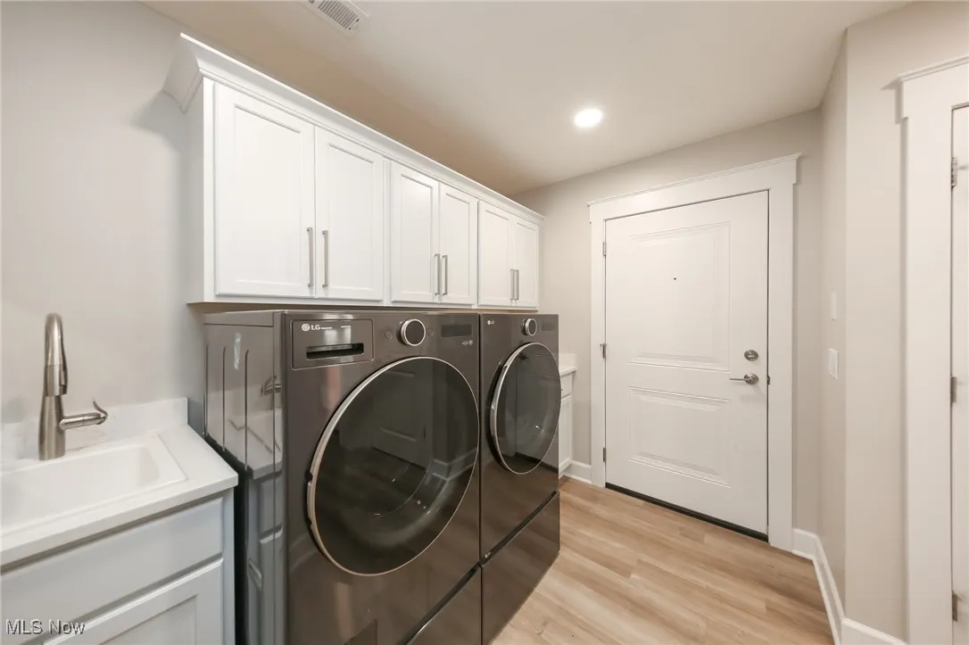 Washroom with light wood-type flooring, independent washer and dryer, recessed lighting, and cabinet space