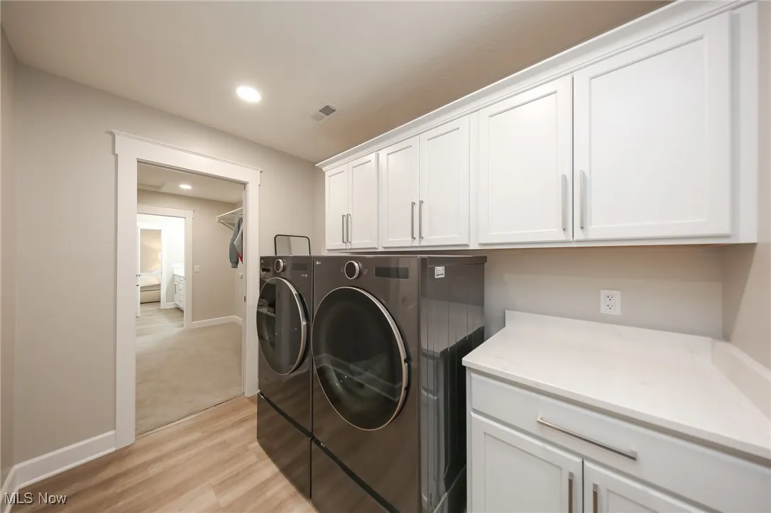 Washroom featuring light wood-style flooring, recessed lighting, washer and clothes dryer, and cabinet space
