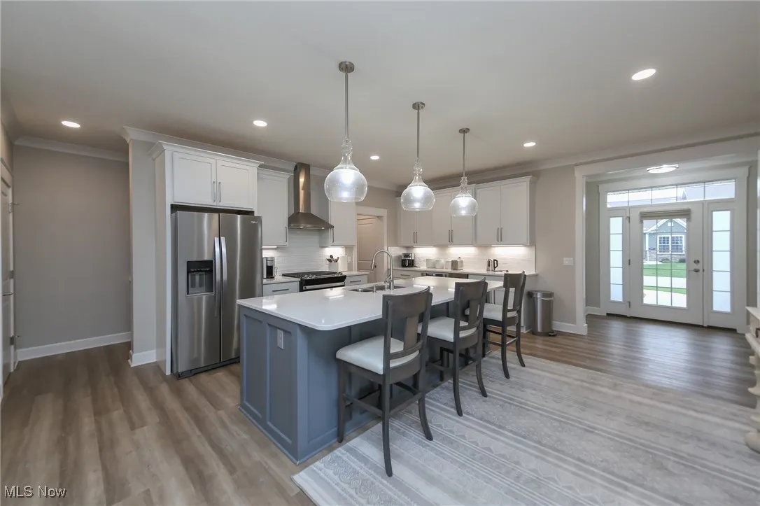 Kitchen with stainless steel refrigerator with ice dispenser, crown molding, white cabinets, a breakfast bar, and an island with sink