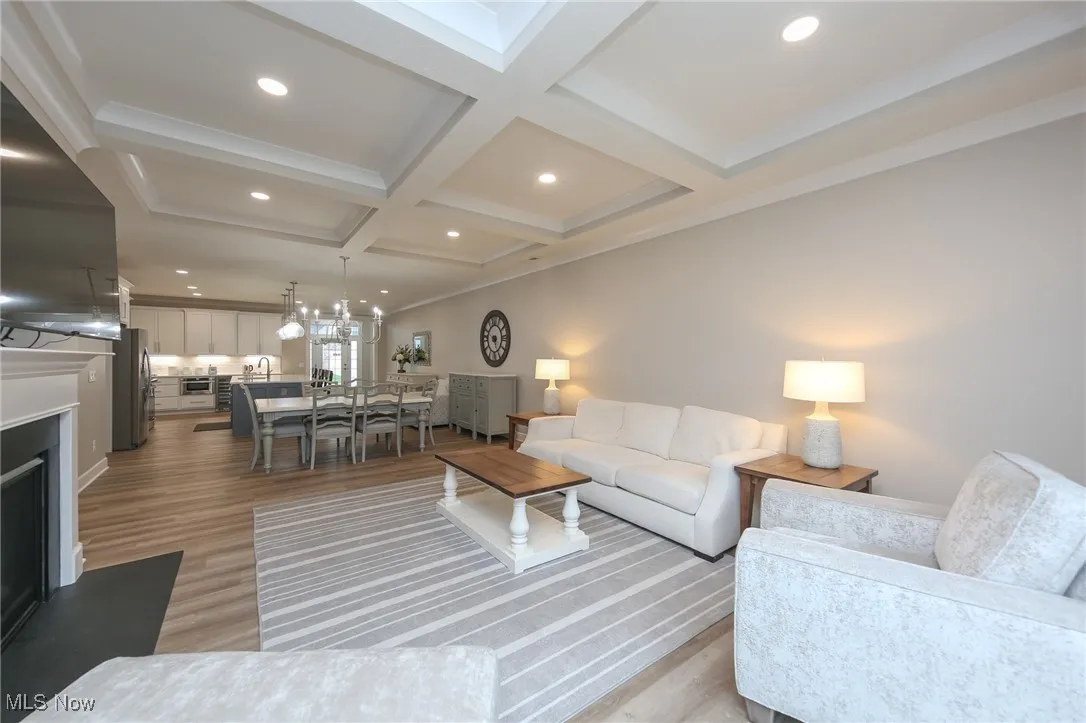 Living room featuring a fireplace with raised hearth, recessed lighting, light wood-style flooring, coffered ceiling, and beam ceiling