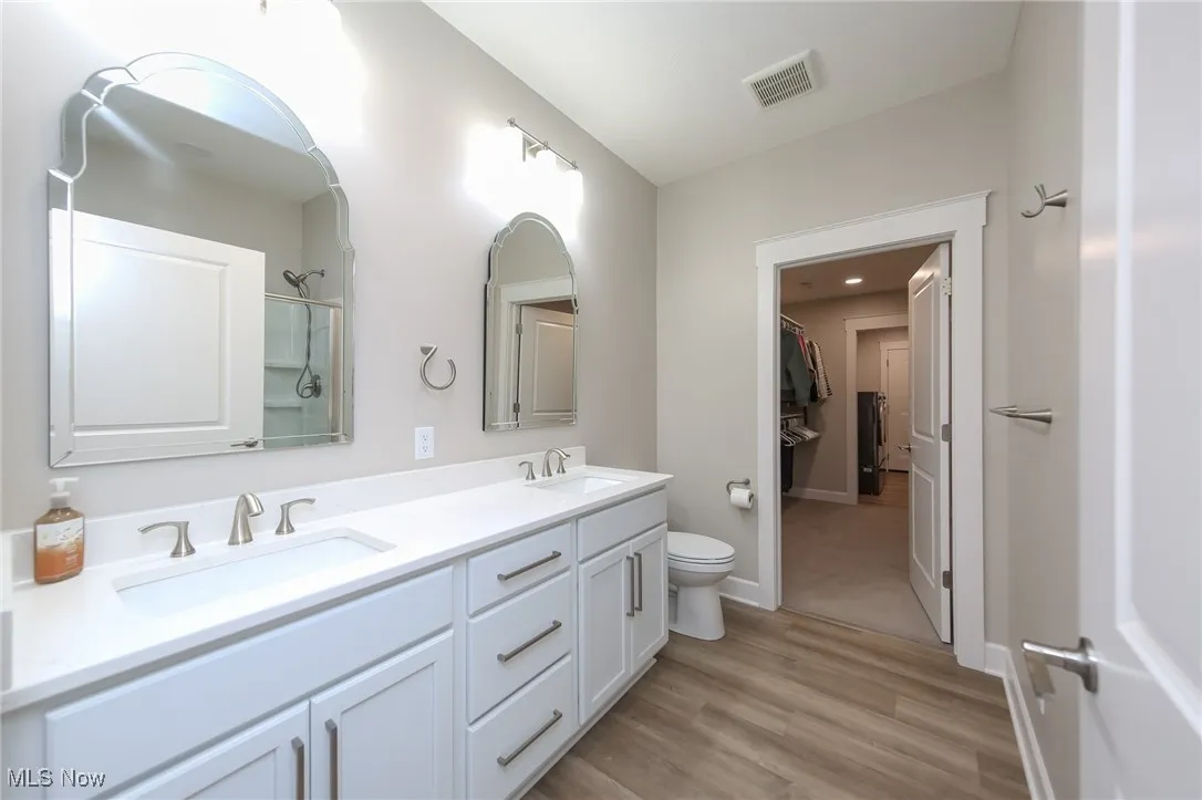 Full bath with double vanity, a walk in closet, light wood-style flooring, and a shower