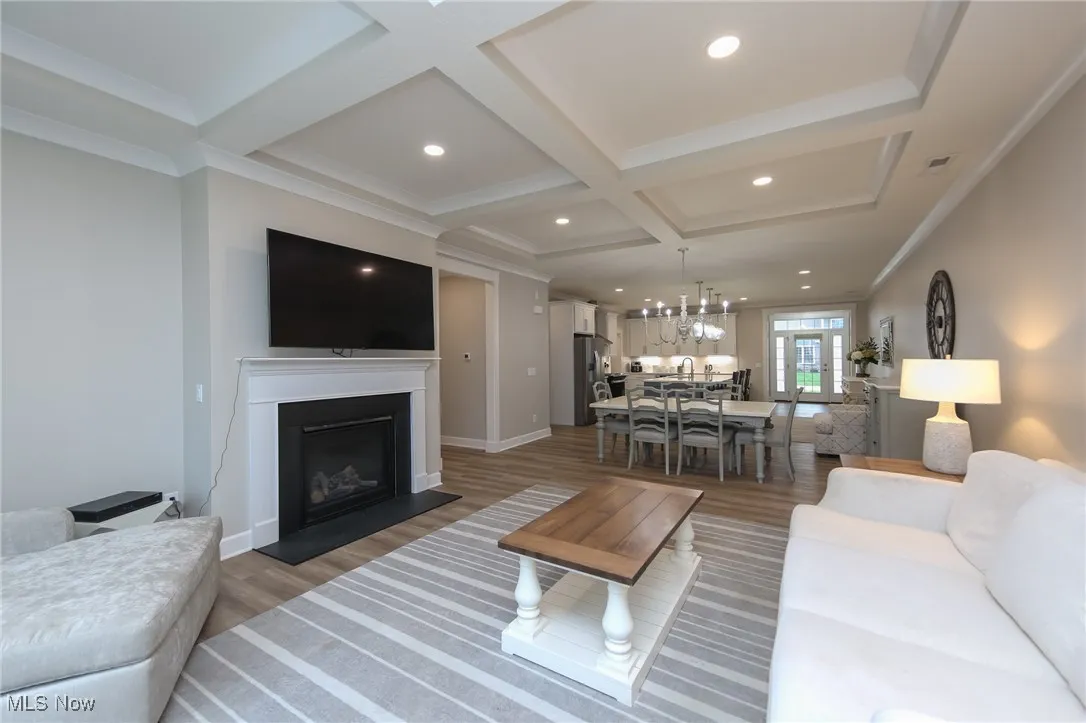 Living area featuring wood finished floors, a fireplace with raised hearth, coffered ceiling, beamed ceiling, and crown molding