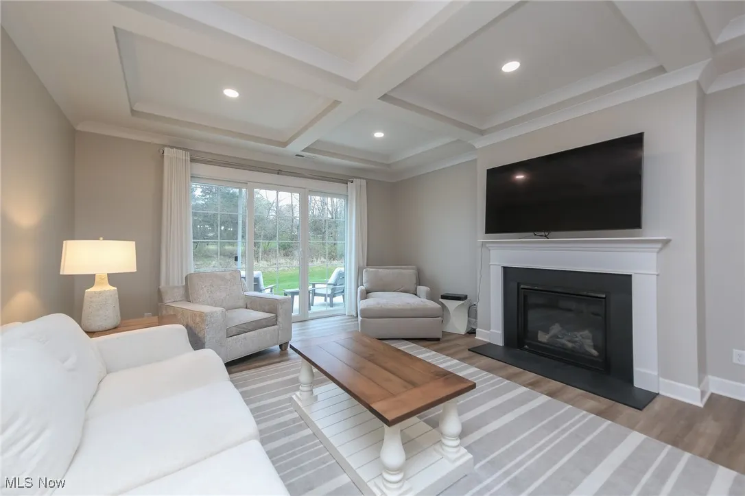 Living room with a glass covered fireplace, beamed ceiling, coffered ceiling, wood finished floors, and recessed lighting