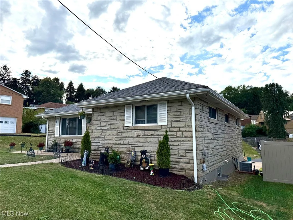 View of front of house featuring stone siding, a front lawn, and roof with shingles